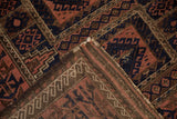 Folded antique Belouch rug corner, madder root and navy geometric compartments, visible pile texture.