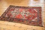 Corner of vintage Hamadan rug, cherry red field, navy Herati motif, wear.