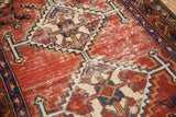 Worn brick red pile and exposed ivory foundation of a vintage Hamadan geometric rug.