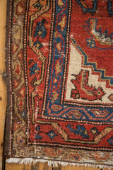 Vintage Hamadan rug corner detail, cherry red and navy geometric motifs, worn pile, visible foundation, ivory fringe.
