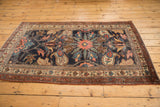 Antique Kurdish Bijar rug corner with worn pile, navy, blush, green oversized floral motifs, patterned border.