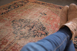 Antique Heriz rug angled view, faded rust and navy diamond medallion, exposed knot heads.