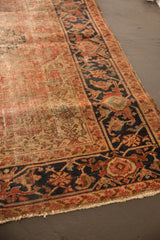 Antique Heriz rug with faded rust field, patterned navy main border, and exposed knot heads.