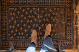 Antique Belouch rug with repeating terracotta and sky blue botehs, showing areas of wear.