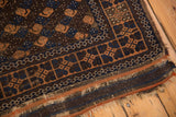 Antique Belouch rug end: worn pile, tattered fringe, navy and terracotta geometric border.