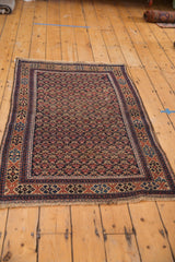 Antique Belouch rug corner: navy trellis floral field, pale terra cotta, sky blue geometric border, fringe.