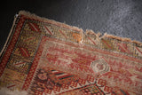 Tattered corner of an antique Caucasian rug with geometric red, ivory, and brown motifs.