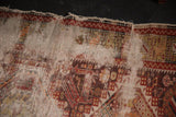 Tattered edge of an antique Caucasian rug with faded geometric patterns and threadbare pile.
