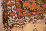 Tattered corner of a vintage Caucasian rug with geometric patterns, exposed foundation.