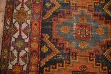 Navy, tangerine, and sky blue geometric patterns on vintage Caucasian rug, wear revealing foundation.