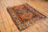 Close-up of the vintage Caucasian rug's corner with tattered fringe and geometric border.