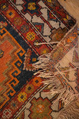 Corner of vintage Caucasian rug with hard tatter fringe, geometric motifs, and visible foundation.