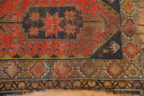 Geometric starburst and hook motifs on vintage Caucasian rug showing worn pile, visible foundation, and tattered fringe.