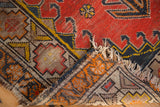 Vintage Caucasian rug corner detail with tattered fringe and geometric pattern pile wear.