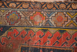 Visible pile wear and tattered edge on vintage Caucasian rug's red, gold, blue geometric border.
