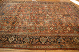 Vintage Mahal carpet corner detailing its distressed chestnut brown field and patterned navy border.