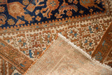 Folded corner of vintage Hamadan rug, revealing navy and copper Herati pattern with woven foundation.