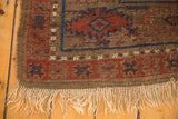 Antique Belouch carpet corner with hand-knotted fringe, geometric design, and visible pile wear.