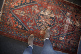 Antique Hamadan rug's dark wine red and navy geometric patterns, showing wear and visible foundation.