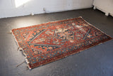 Antique Hamadan rug's geometric pattern in deep red and navy, with visible pile wear.