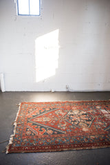 Angled view of antique Hamadan rug end with geometric vine motifs and worn fringe.