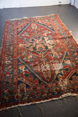 Antique Hamadan rug corner detail, dark wine red and navy geometric motifs, visible foundation, tattered ends.