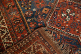 Folded vintage Afshar rug corner, showing geometric pinwheel patterns, low pile, and natural fringe.