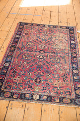Antique Kerman rug corner detail: cochineal red floral vinery field, navy border, visible wear.