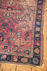 Storied antique Kerman rug: cochineal red field, sprawling vinery, navy border, tattered edge.