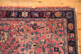 Kerman rug corner detail: tattered edge, navy floral border, cochineal red vinery field.