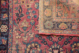 Antique Kerman rug close-up showing worn cochineal red floral field, navy border, and hand-knotted reverse.