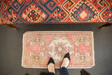Distressed vintage Oushak rug end, with raspberry red, ivory, and plant motif on worn pile.