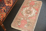 Distressed vintage Oushak rug corner showing raspberry red, ivory plant motifs and fringe.
