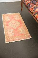 Distressed Oushak rug corner with pale pink field, subtle ivory pattern, and secured white fringe.