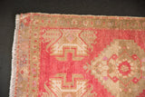 Vintage distressed Oushak rug corner, showing worn dusty raspberry pile and geometric border.