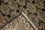 Distressed Oushak rug corner showing black, apricot geometric patterns, worn pile, and exposed foundation.