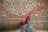 Overhead view of distressed Oushak rug with faded raspberry and silver floral medallion.