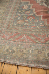 Fringed end of distressed Oushak rug, showing low pile with faded raspberry and bronze motifs.