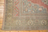 Faded floral spandrel, intricate borders, and fringed edge on a distressed Oushak rug.