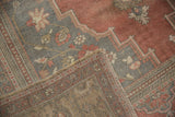 Distressed Oushak rug corner showing low pile, muted floral motifs, and hand-knotted reverse.