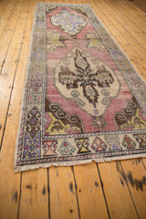 Distressed Oushak runner end, with mauve field, geometric border, fringe, and worn texture.