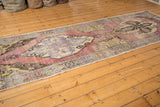 Vintage distressed Oushak runner with faded mauvy-pink field, lupine blue details, and visible wear.