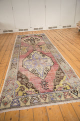 Distressed Oushak runner end: worn mauve field, fringe, and multicolored patterned border.