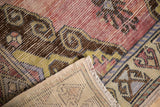Vintage distressed Oushak rug corner with visible wear, exposed light foundation, and fringe.