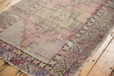 Low pile texture of a distressed Oushak runner's serrated geometric border in mauve and gold.