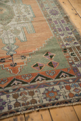 Distressed Oushak rug border displays apricot, sage, and aubergine floral palmette motifs.