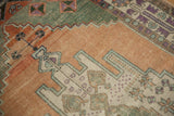 Worn texture of distressed Oushak rug: apricot, sage, purple geometric border, pinwheel elements.