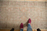Distressed Oushak runner's worn pile, highlighting peach, ivory, and bright pink floral motifs.