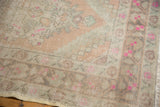 Close-up of distressed Oushak rug corner, showing pile wear, peach, ivory, and vivid pink patterns.