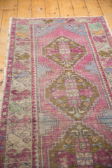 Distressed Oushak runner showing soft pink, blue, and bronze geometric patterns with aged pile texture.